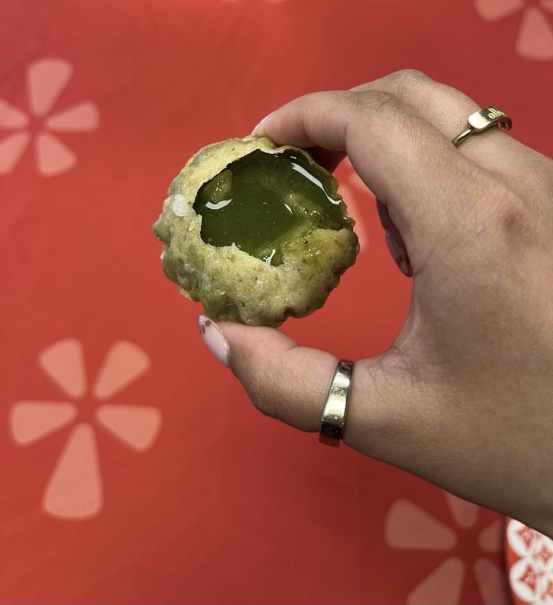 A pistachio cookie held over a red plate