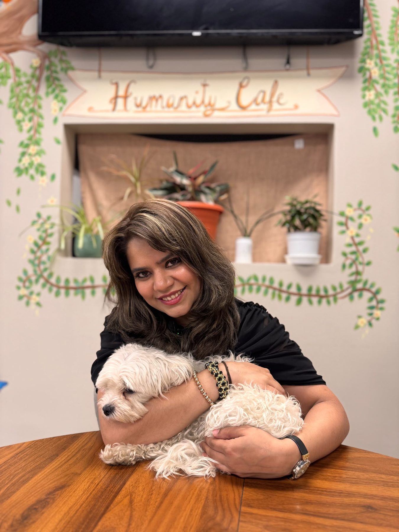 Amrin with the café dog at the table beneath the Humanity Café mural